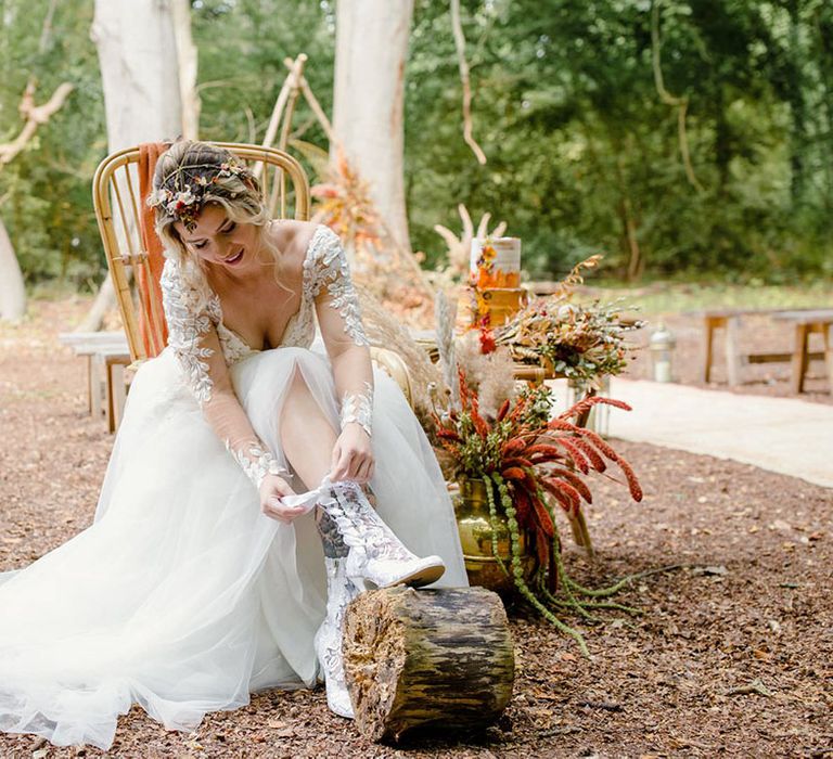 Bride in long sleeved v neck soft ivory dress with lace floral detailing on the bodice and sheer sleeves tying up ivory embroidered bridal boots with white lace fastening 