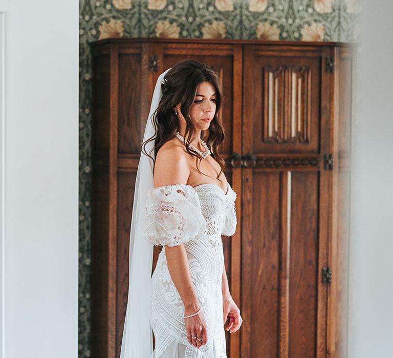 Bride in boho fitted lace wedding dress with detachable sleeves with curled brown hair in a half up half down hairstyle 