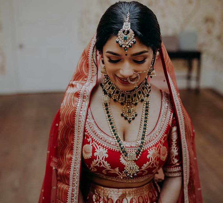 South East Asian bride wears gold jewellery and red and gold lehenga complete with intricate bridal henna 