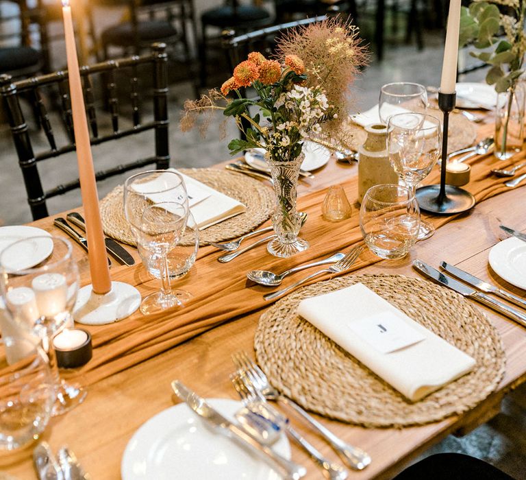 Orange fabric table runner to the middle of wooden banquet tables finished with black candle holders 