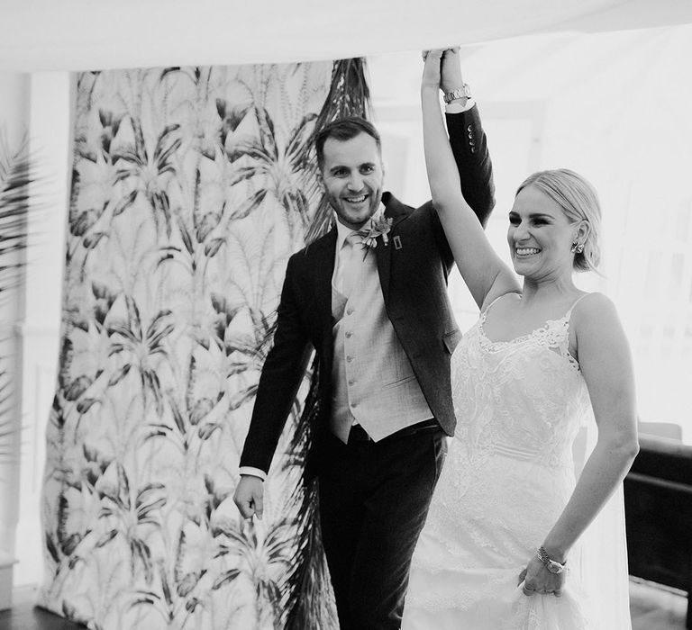 The bride and groom enter their wedding marquee reception together with their hands raised in the air 