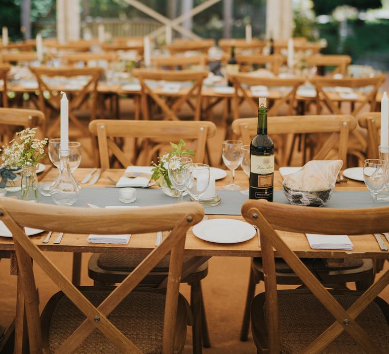 Long wooden wedding tables with blue table runners and bud vases full of daisies in marquee reception at Badgers Holt 