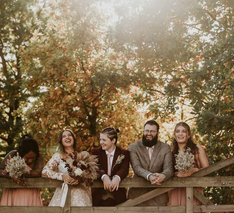 Wedding party with dried flower autumnal bridal bouquets standing on a wooden fence at Bassmead Manor Barns wedding venue 