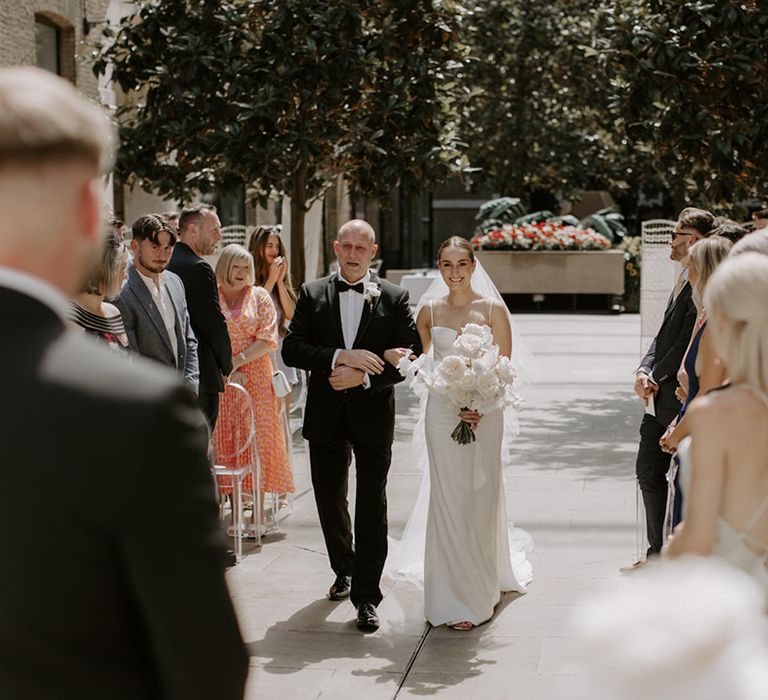 Father of the bride in black tie walks the bride down the aisle at London city wedding with modern minimalist styling 