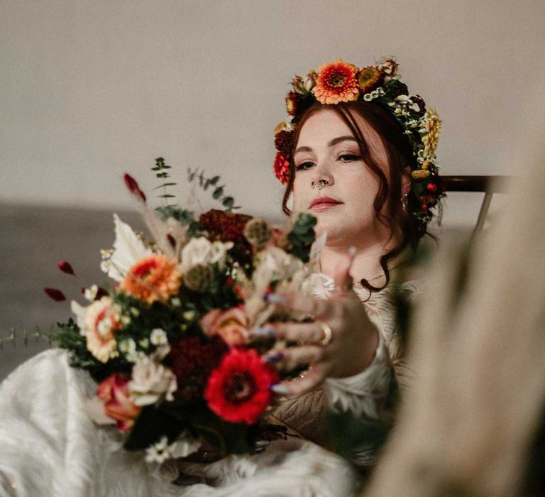 Bride holding earthy toned garden rose, pampas grass, dried flower and foliage bridal bouquet sitting on crushed velvet olive green loveseat 