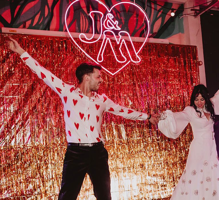 The bride and groom share a dance on the stage with gold streamer decorations and personalised neon sign