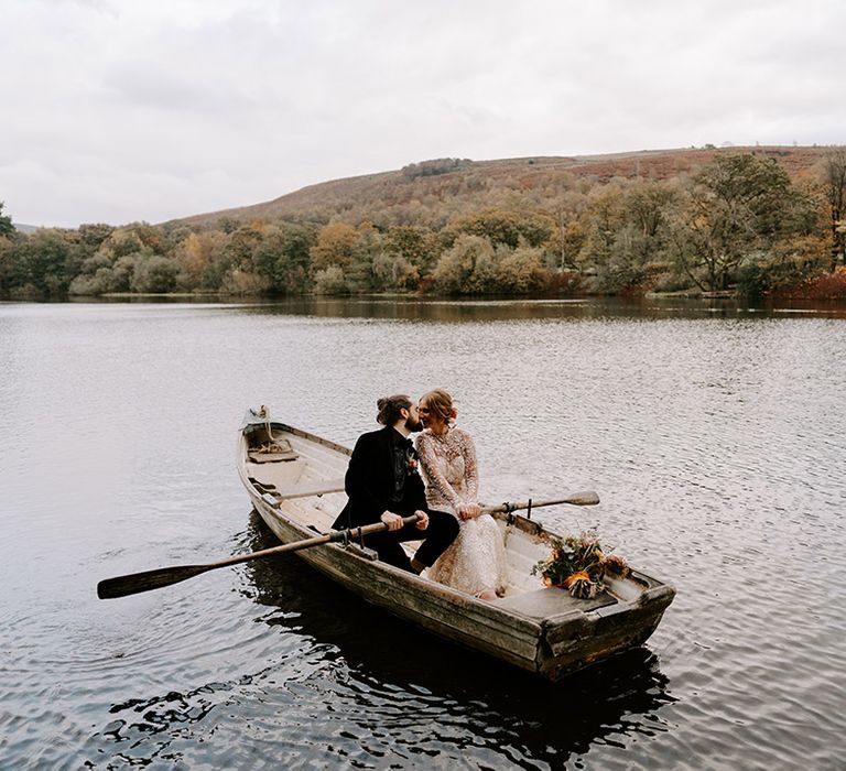 The bride in a boho lace wedding dress with long sleeves rides in a boat with the groom 