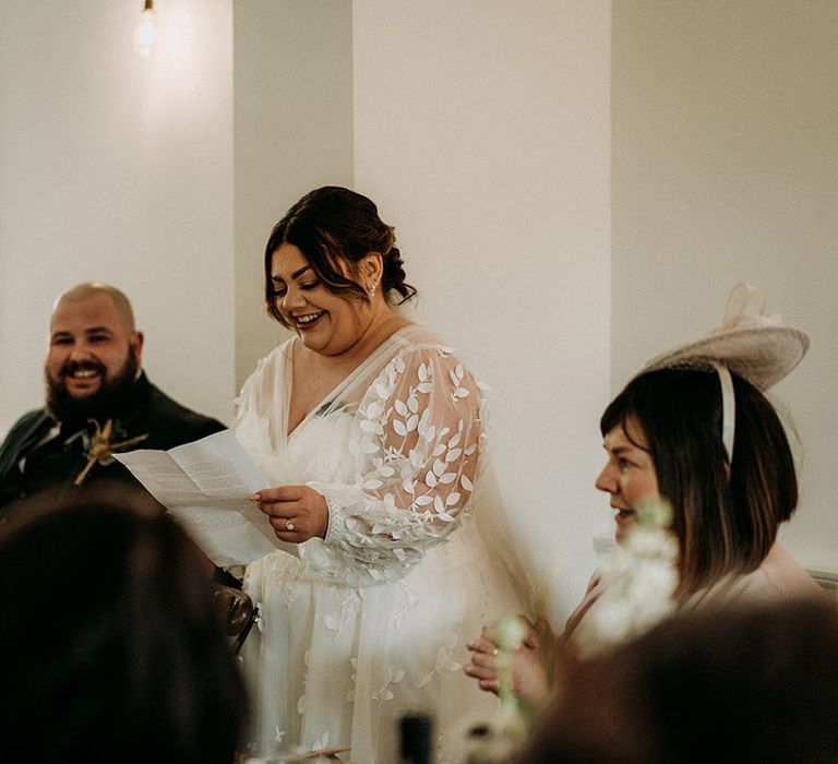 Bride in long sleeve lace wedding dress by All Who Wonder reading out her bridal speech 