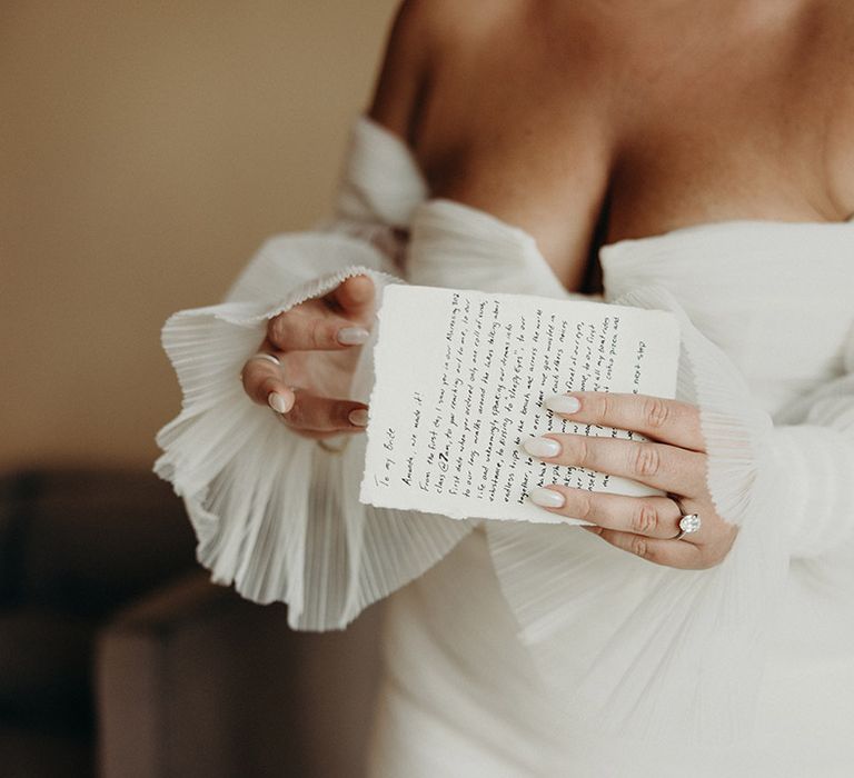 bride in a strapless wedding dress holding a letter from her groom showing off her white wedding nails and oval diamond engagement ring 