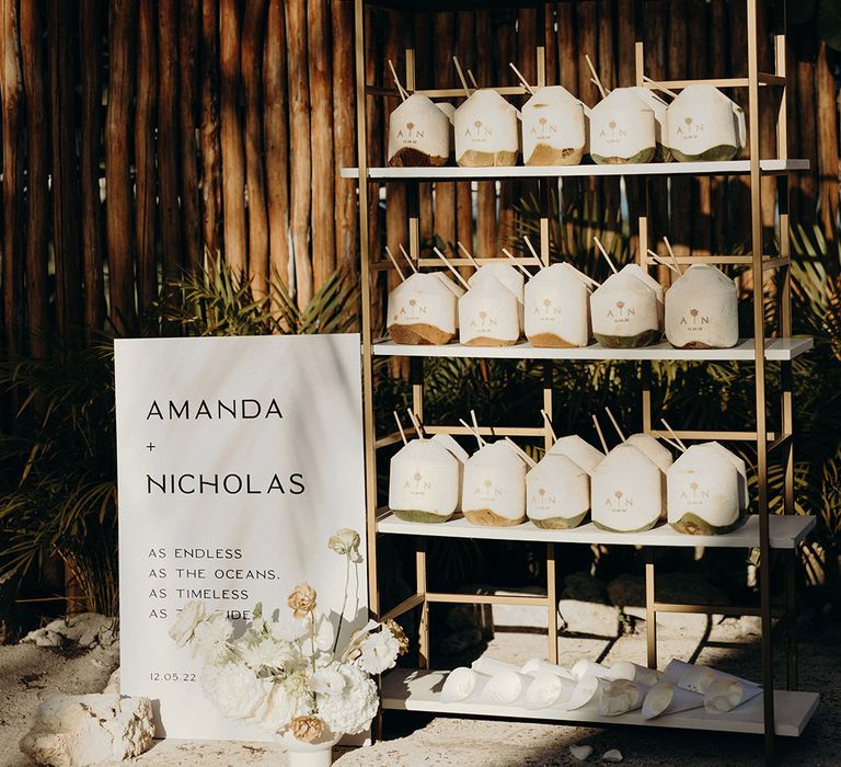 Stand of coconut drink wedding favours with bespoke gold monogram decoration for Mexico beach wedding 