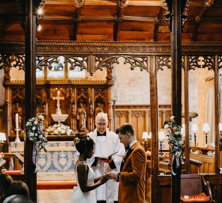 Groom wearing crushed burnt orange velvet grooms blazer standing with bride in v-neck sleeveless wedding dress with 3D floral applique train at Brinsop Court wedding