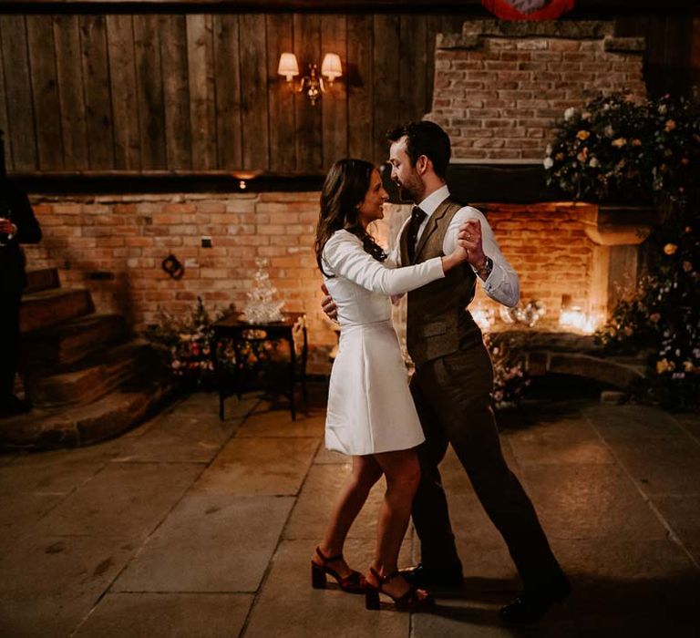 Bride in long sleeve short wedding dress and red velvet chunky wedding heels doing choreographed wedding first dance with groom in brown waistcoat and suit trousers 