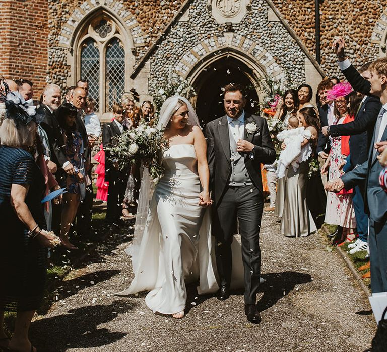 The bride and groom walk hand in hand as they exit from their church wedding ceremony 