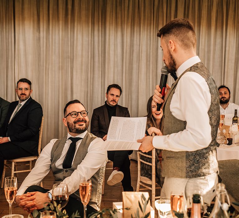 The groom stands in his waistcoat to deliver his wedding speech 