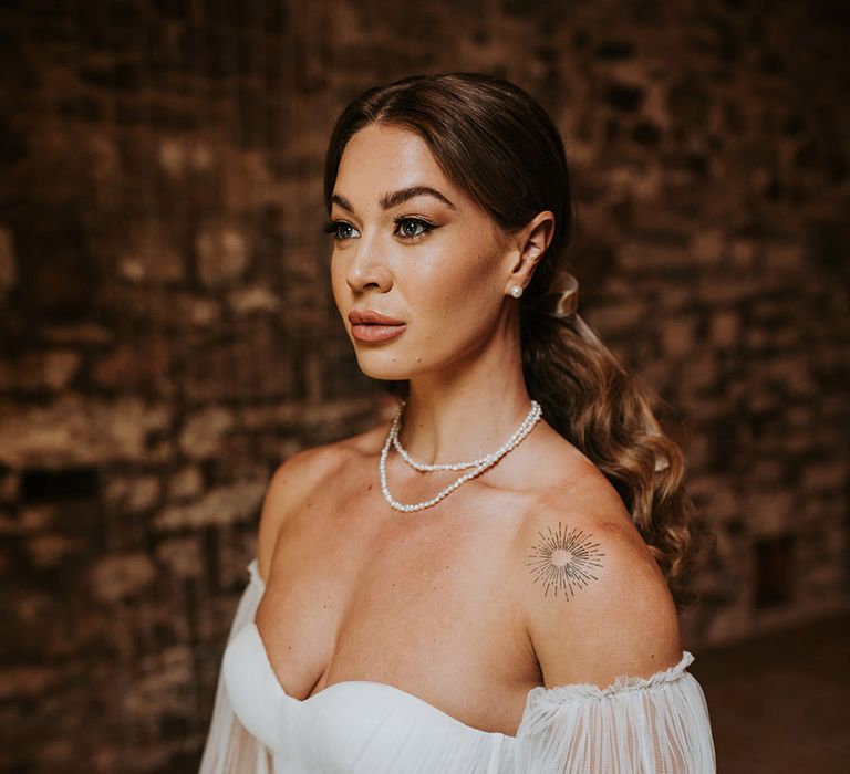 The bride wears an off the shoulder wedding dress with pearl jewellery 