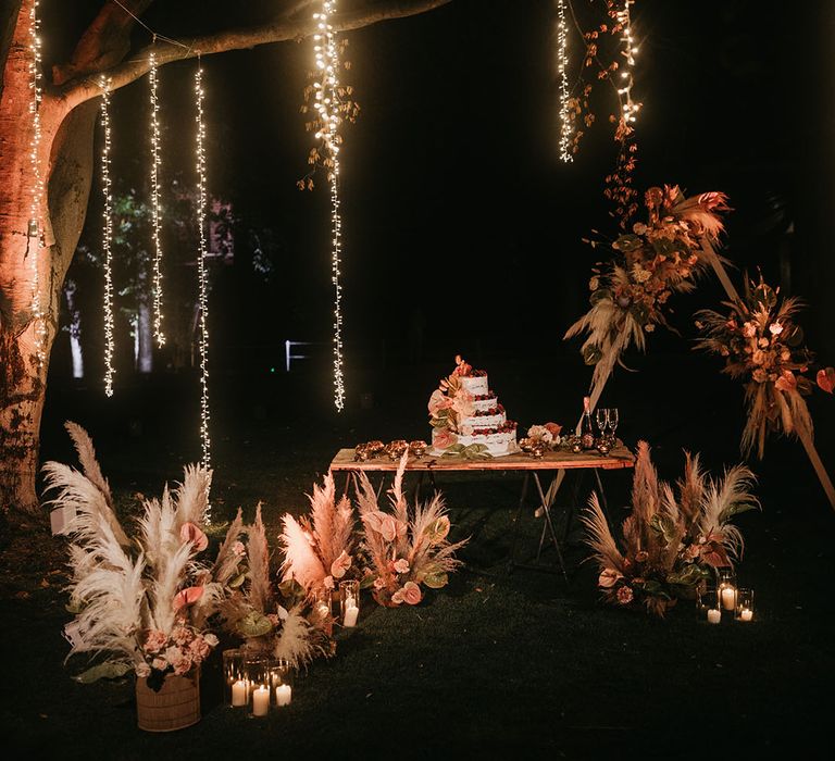 wedding cake table with boho flower arrangements and string lights 