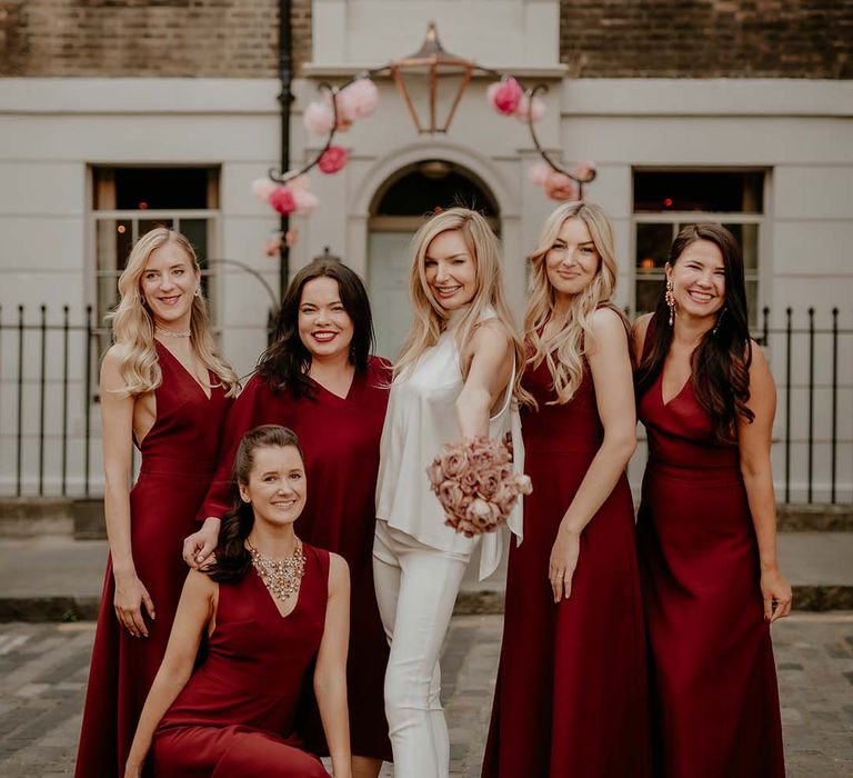 Bridal party in burgundy bridesmaid dresses with bride in trousers and top outfit for city wedding in London