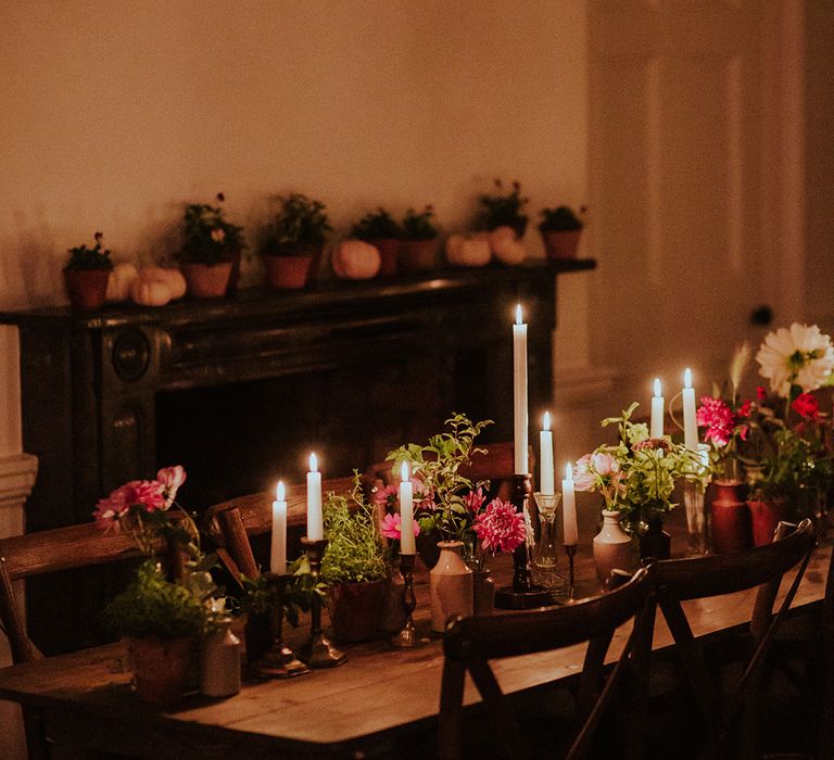 Cosy tablescape with white candles of different sizes are lit surrounded by pink and red wedding flowers 