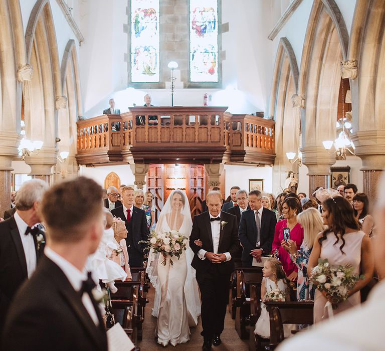 Traditional church wedding ceremony with the bride being walked by the father of the groom down the aisle 