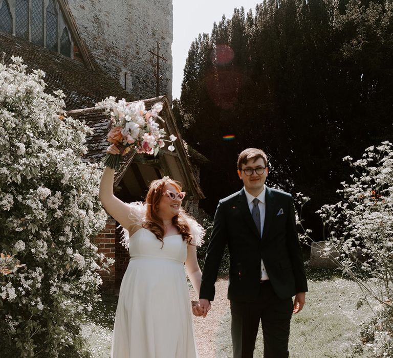 Bride in feather wedding dress with sunglasses posing with the groom 