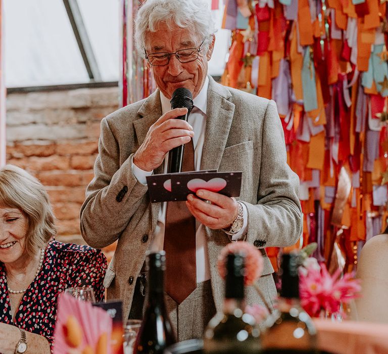 Father of the bride in beige suit stands up to read out his wedding speech 