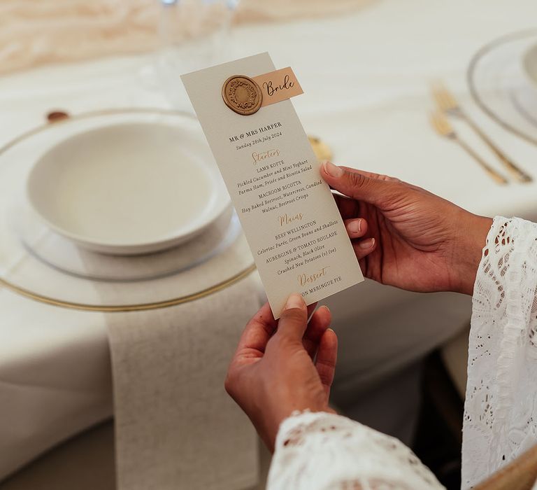 Bride reading white wedding menu with gold wax seal for luxury wedding 