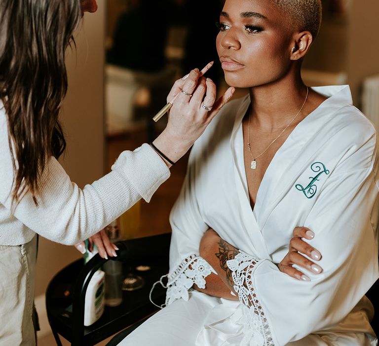 Bride in white satin robe getting makeup done for the wedding day