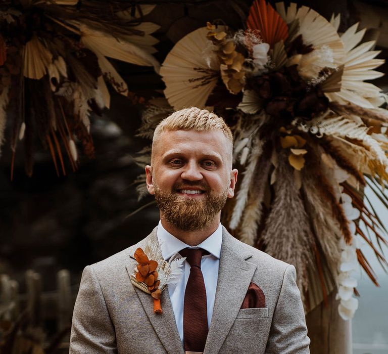 Groom in a grey wedding suit with brown tie and tie clip with boho dried wedding flower buttonhole 