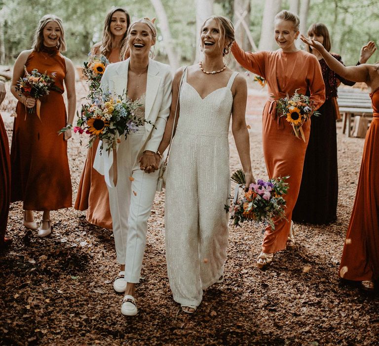 Bridal party wearing burnt orange satin bridesmaid dresses with the two brides for group wedding photo 