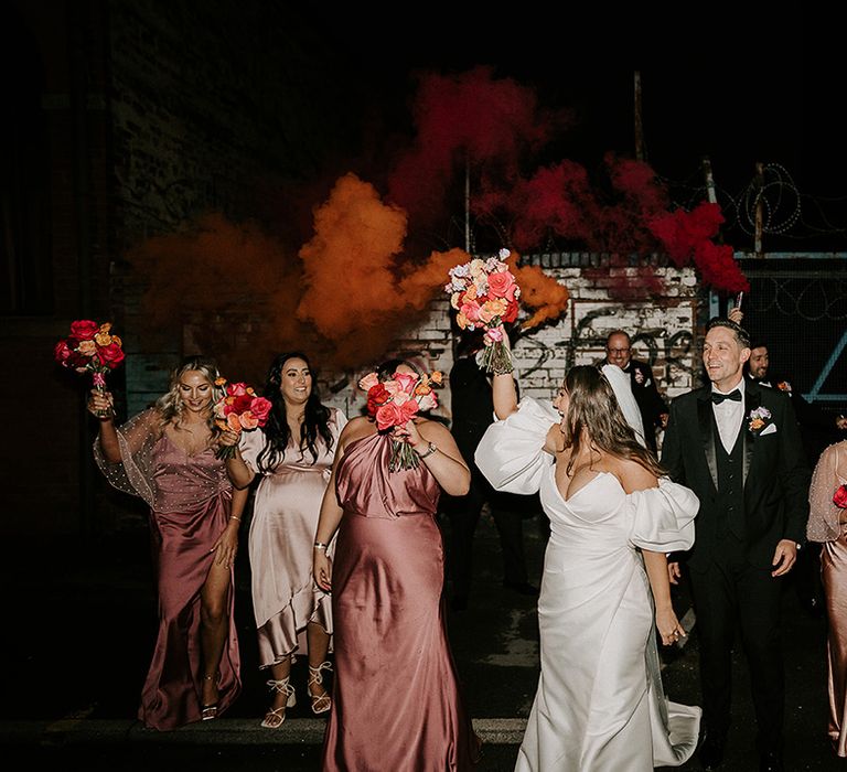 Flash photo of the wedding party posing together in pink wedding outfits with bright bouquets and smoke flares 