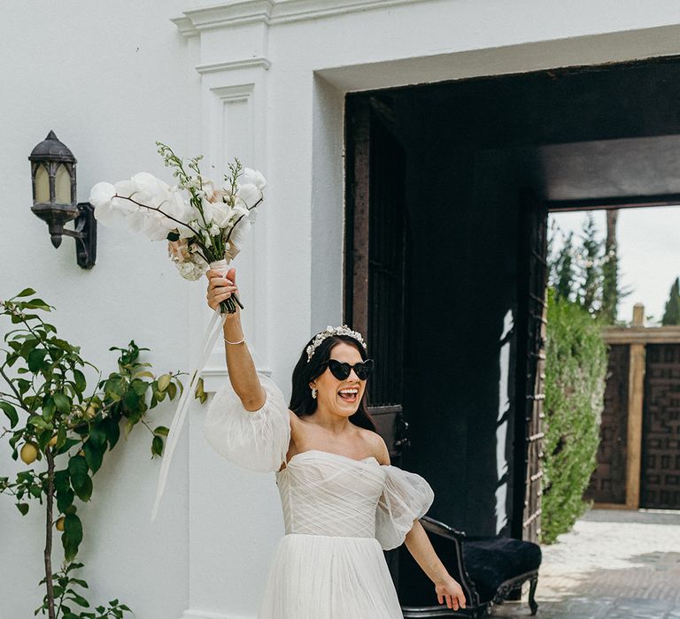 Bride in strapless wedding dress with detachable puff sleeves with heart shaped sunglasses and a floral headband 