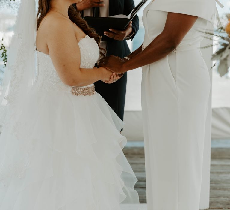 Black bride and bi-racial bride holding hands during their LGBTQ+ wedding ceremony 