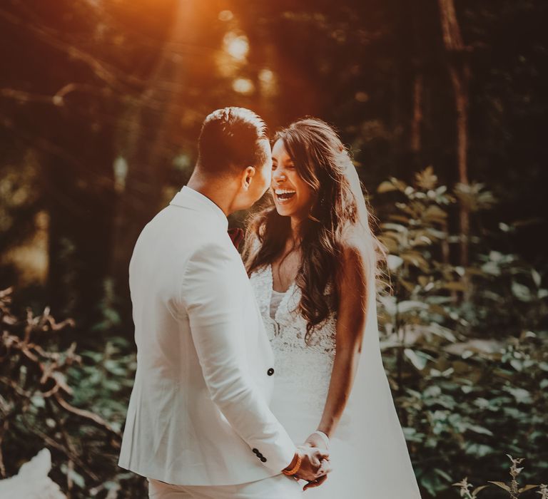 Bride & groom hold hands outdoors with light behind them