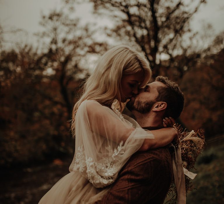 Bearded groom in wool jumper picking up his bride and kissing her in a floaty chiffon wedding dress 