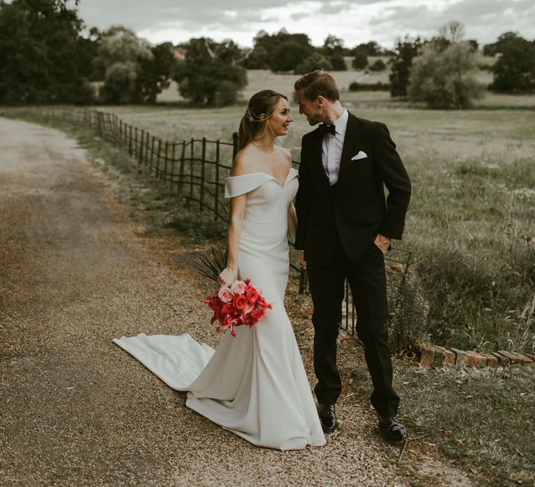 Bride & groom walk down countryside pathway whilst holding coral bouquet