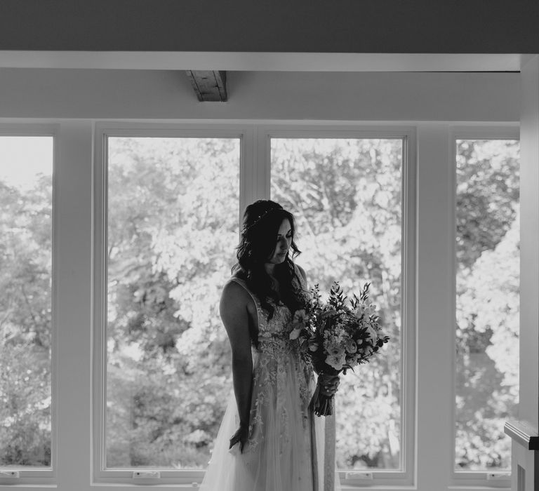 Bride stands in front of window on the morning of her wedding