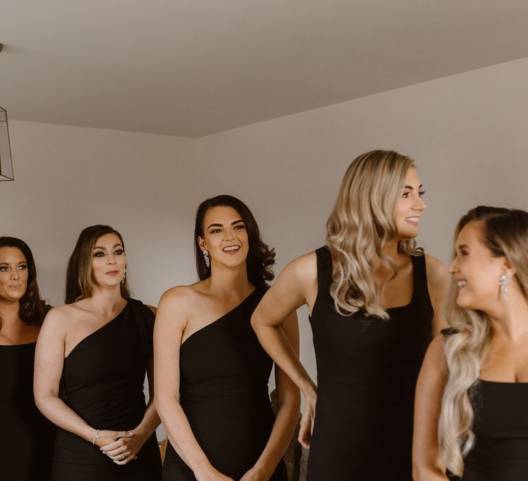 Bridesmaids with curled hair and black bridesmaids dresses stand with father of the bride in black tuxedo before the wedding