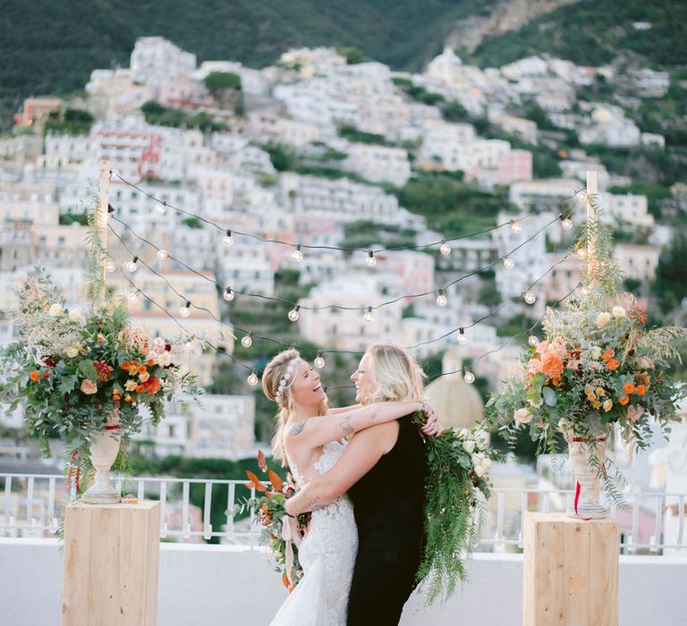 The brides hugging and laughing at the altar of their outdoor Italian wedding ceremony