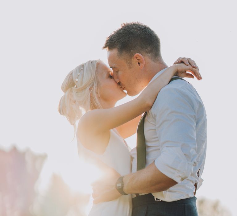 Bride & groom kiss as the sun streams through the trees