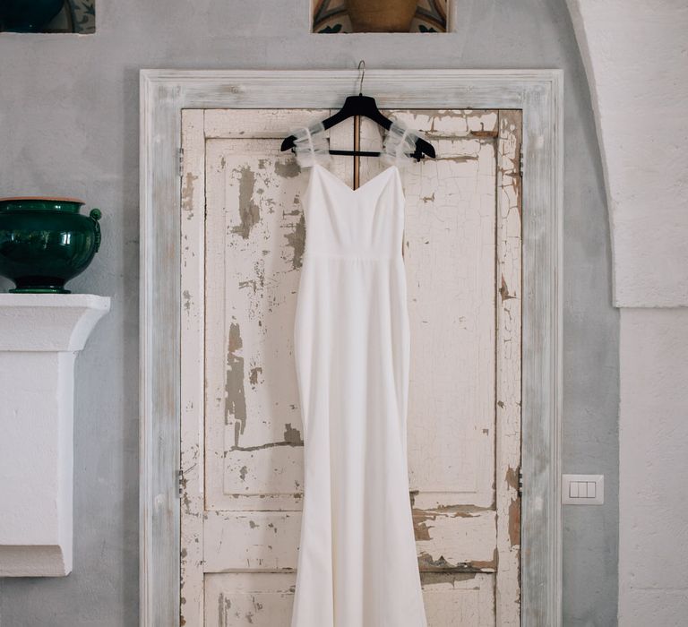 Minimal Halfpenny London wedding gown with ruffle straps hanging up