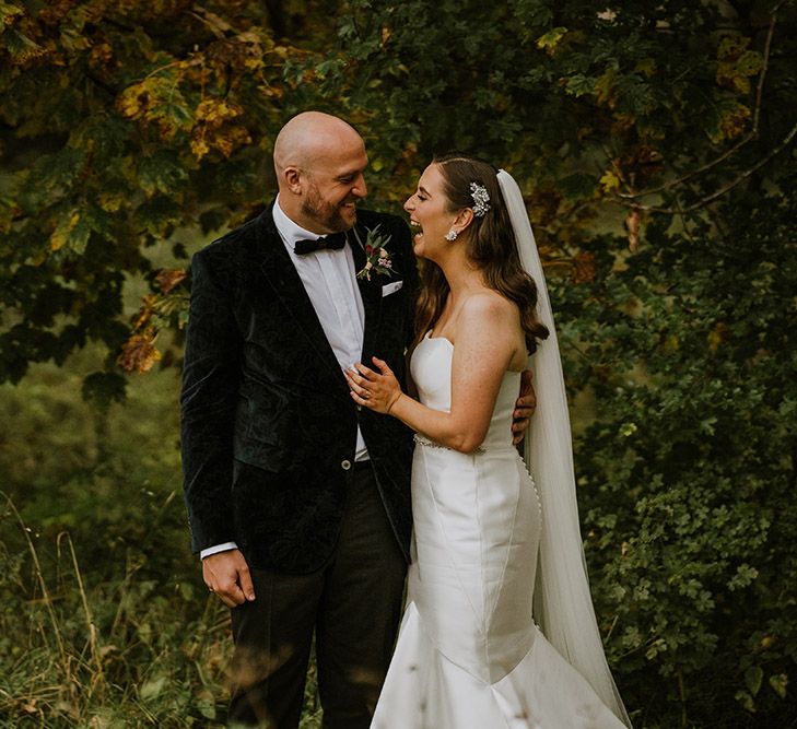 Bride in a strapless wedding dress with fishtail laughing with her groom in a velvet tuxedo jacket 