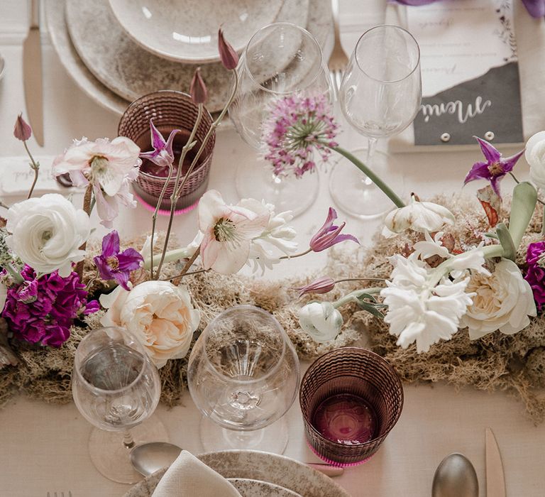 Place setting with speckled tableware, purple glasses and wedding flowers 