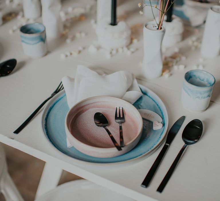 Place setting with pastel pink and blue tableware and black cutlery 