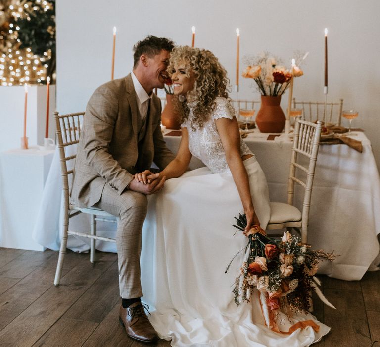 Groom whispering in bride's ear at their white wedding table set up with neutral tones