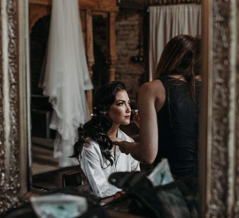 Bride in white satin pyjamas having her makeup done