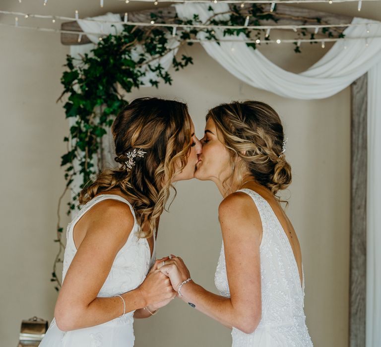 Brides kiss during wedding ceremony whilst holding hands 