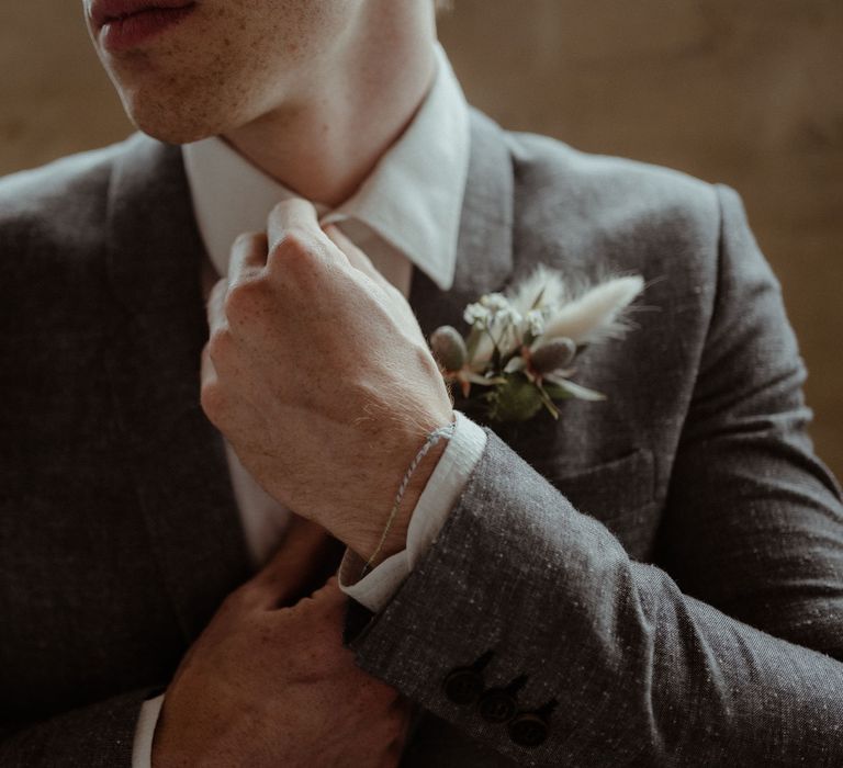 A groom straightens his tie. He wears a grey Japanese cotton suit. 