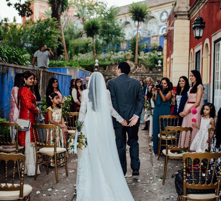 Bride walks down the aisle whilst wearing Pronovias wedding gown and wedding guests look on 