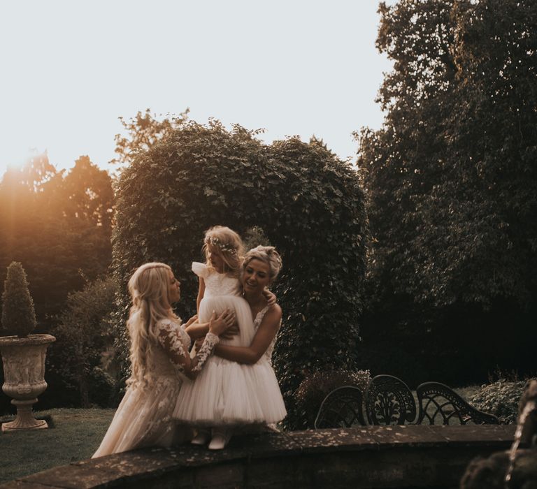 Two brides cuddle their daughter at sunset around a fountain at Crab & Lobster Fairytale Wedding.