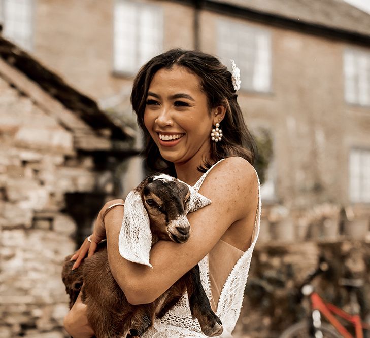 Black bride in a fitted wedding dress with straps holding a goat at their farm wedding venue